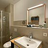 Bad mit ebenerdiger Dusche, Toilette, Spiegel und Wasch-Becken.