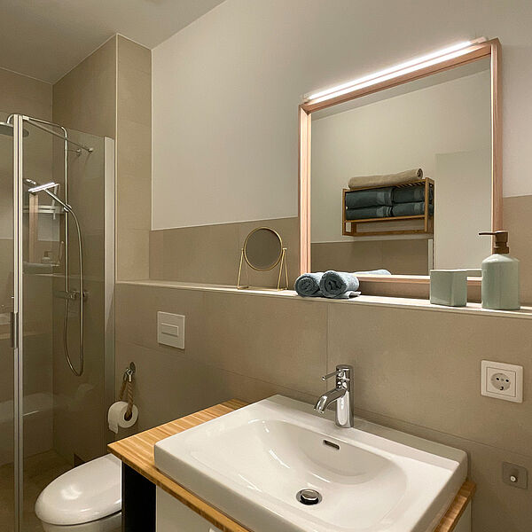 Bad mit ebenerdiger Dusche, Toilette, Spiegel und Wasch-Becken.