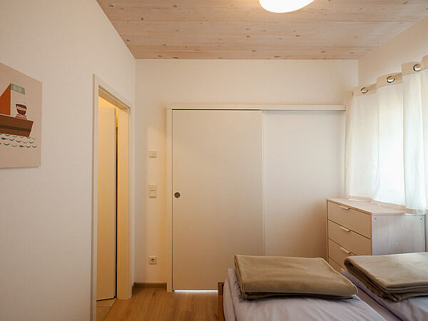 Gemütliches Schlafzimmer mit Blick vom Bett auf die geschlossene Schiebetür zum Wohnzimmer. Links ist die Tür zum Bad geöffnet. 