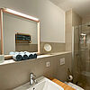 Creme-farbiges Bad mit Glas-Dusche, Becken, Toilette und Spiegeln.