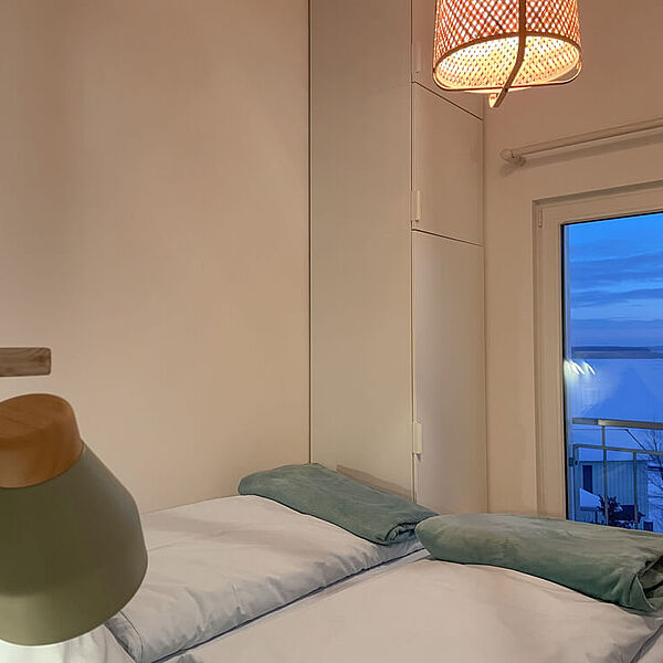 Schlafzimmer mit Doppelbett und bodentiefem Fenster.