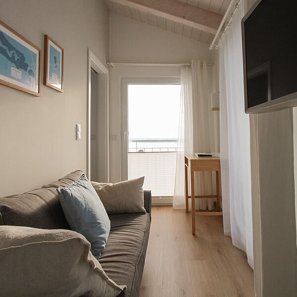 Couch mit Kissen im Wohnbereich. Rechts ein Fernseher an der Wand.