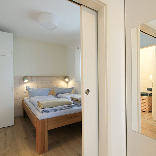 Blick durch die Schiebetür ins das gemütliche Schlafzimmer mit Doppelbett. Vor der Tür hängt auf der rechten Seite ein Spiegel an einer Schrankseite..