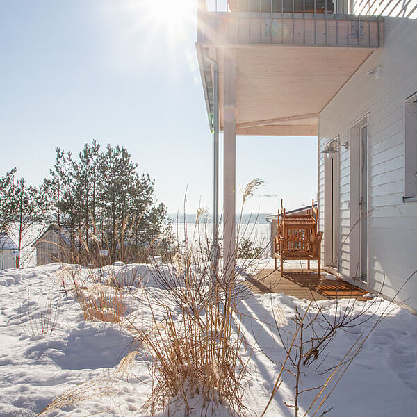 Garten mit Schnee in der Sonne mit Blick auf den Hainer See. Rechts eine Hauswand, und eine Terrasse unter einem Balkon.