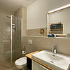 Bad mit Glas-Dusche, Toilette, Spiegel und Wasch-Becken.