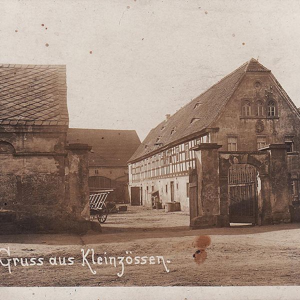 Schwarz-weiß-Foto eines alten Fachwerkhofs mit offenem Tor. Darauf geschrieben "Gruss aus Kleinzössen".