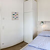 Schlafzimmer mit Kleiderschrank und Doppelbett rechts. Auf der linken Seite ist eine geöffnete Tür zu einem Badezimmer mit Waschbecken..