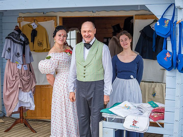 Drei Kostümierte zwischen Kleidung und Taschen