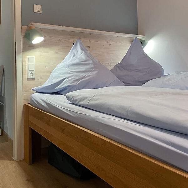 Doppelbett mit eingeschalteten Bettlampen und großen Kopfkissen.