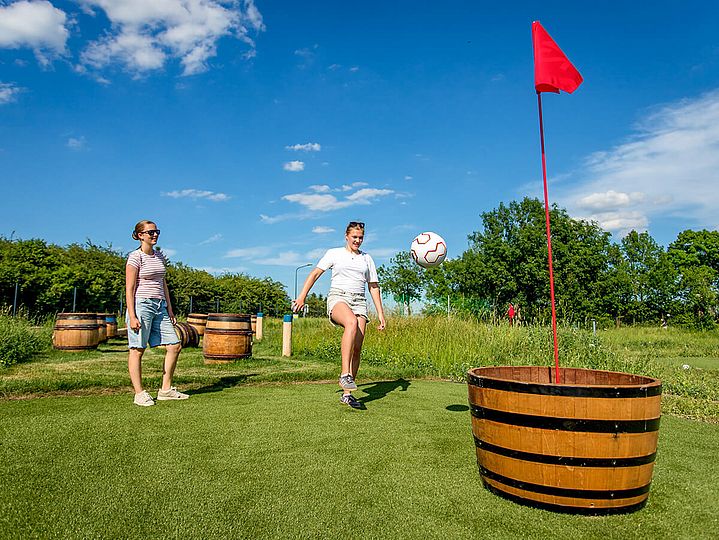 2 Frauen kicken einen Ball in eine Holztonne