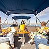 Fünf Freunde auf einem Boot mit Sonnenverdeck. In der Mitte steht ein Eimer mit Champagnerflaschen.