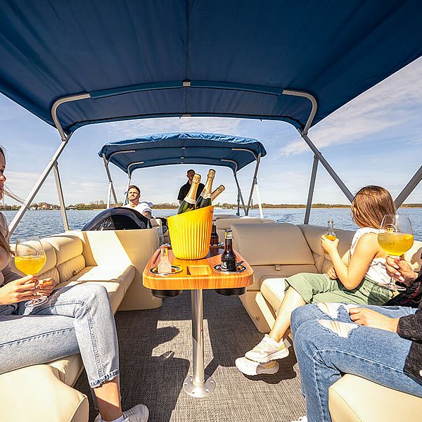 Fünf Freunde auf einem Boot mit Sonnenverdeck. In der Mitte steht ein Eimer mit Champagnerflaschen.