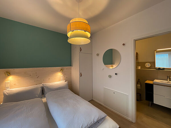 Schlafzimmer mit Spiegel und Bett. Rechts führt eine Tür ins Badezimmer.