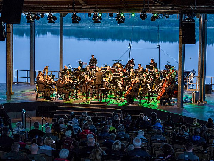 Orchester zur blauen Stunde auf einer Bühne, im Hintergrund der See
