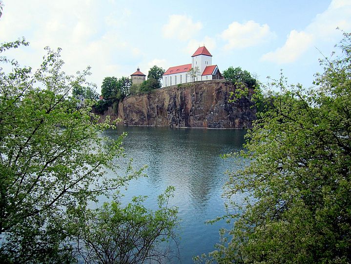 Kirche auf einem Fels vor einem Steinbruchsee