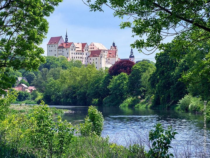 Schloss auf bewaldetem Hügel über einem Fluss