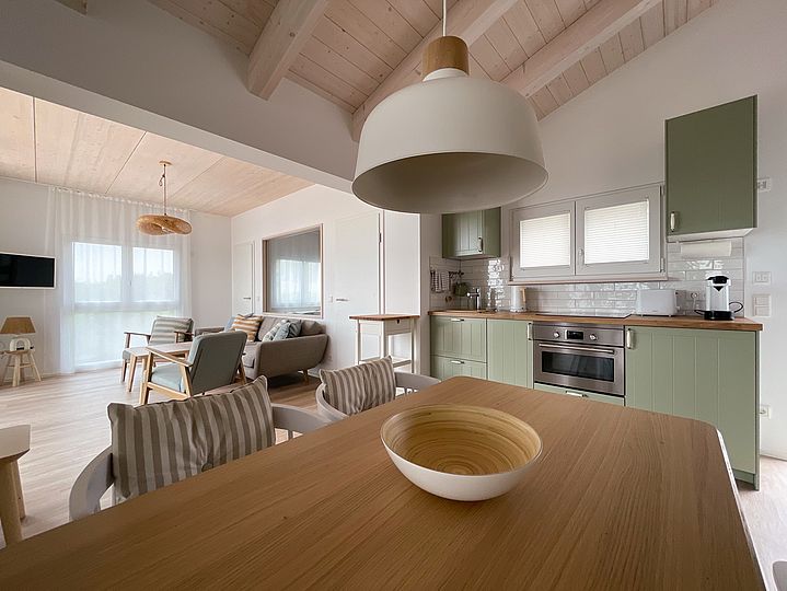 Ess-Tisch mit Holz-Schale und Blick aufs Sofa und die Küchen-Zeile.