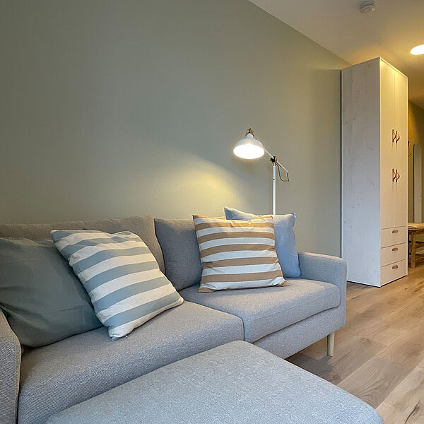 Kuscheliges Sofa im Wohnzimmer. im Hintergrund rechts führt ein Gang zur Eingangstür ab. Im Flur steht ein Schrank.