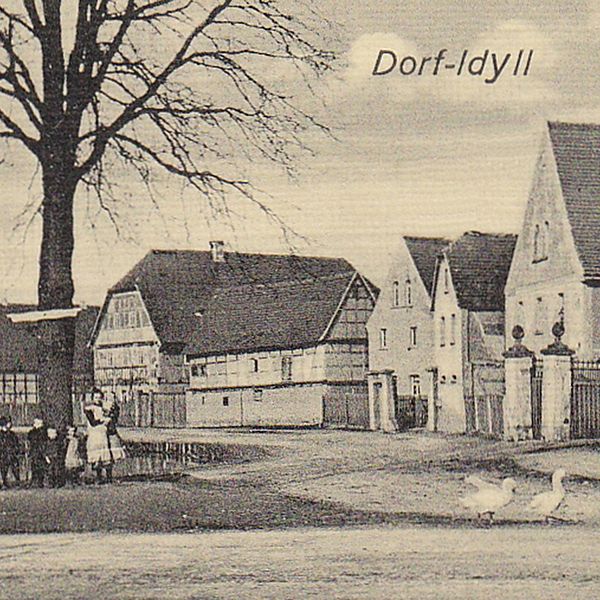  Schwarz-weiß Ansicht vom Dorf. Titel: Dorf-Idyll. Links Menschen unter einem Baum, rechts ein paar Gänse und Fachwerkhäuser.