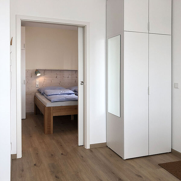 Blick durch die offenen Tür vom Wohnzimmer in das gemütliche Schlafzimmer. Auf der rechten Seite steht ein Schrank mit Spiegel.