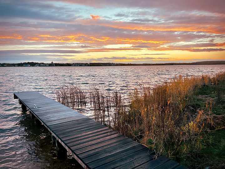 Nasser Steg neben grünem Ufer im Sonnenuntergang