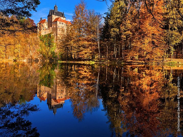 Bunter Wald am Fluss, auf einem Hügel thront Burg Kriebstein