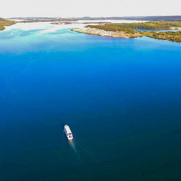 Vogelperspektive auf das blaue Wasser eines Sees, in der Mitte fährt ein Personenschiff. Am Rand des See sind Inseln zu erkennen.