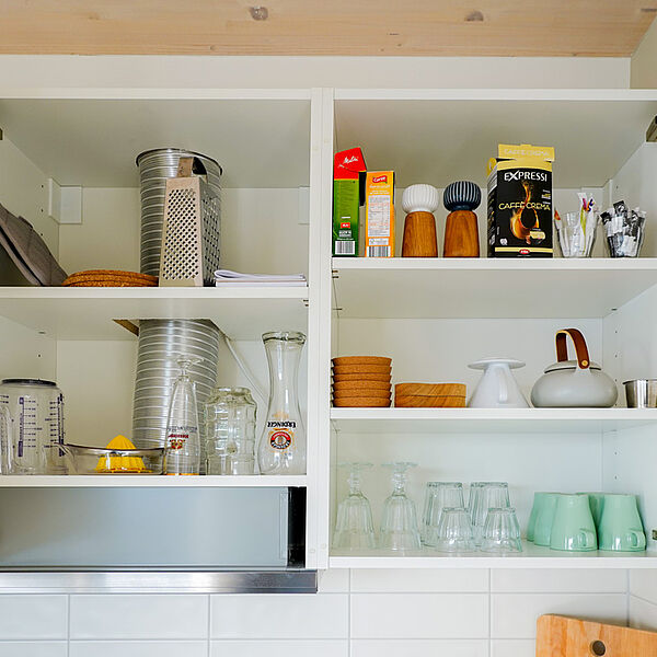 Geöffneter Küchen-Hängeschrank mit Tassen, Gläsern und Küchenutensilien