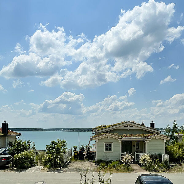 Straße mit Häusern, dahinter der blaue Hainer See.