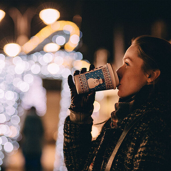 Frau trinkt Heißgetränk am Weihnachtsmarkt