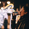 Frau trinkt Heißgetränk am Weihnachtsmarkt