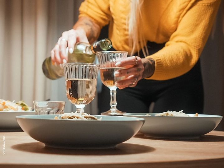 Frau gießt zwei Weingläser ein über gedecktem Tisch