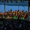 Eine Bühne mit Orchester im blauen ABendlicht, dahinter direkt der Schladitzer See.