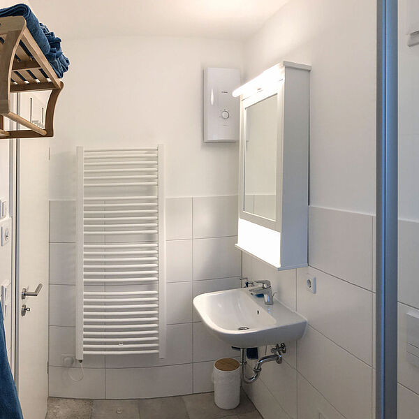 Wohnung 3: Bad mit Waschbecken, Spiegel und Handtuchheizkörper.