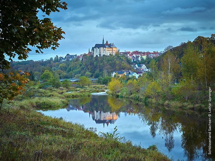 Burg auf Hügel vor einem Fluss mit Auen