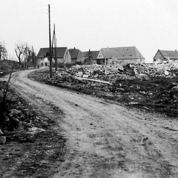Schwarz-weiß-Foto von eine Straße, an den Ränden sieht man Schutthaufen, in der Ferne stehen noch ein paar Häuser