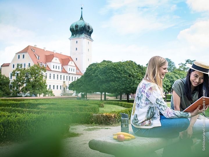 Zwei Frauen sitzen im Schlossgarten vor Schloss mit Zwiebeldach
