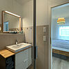 Bad: Wasch-Becken, Badezimmer-Schrank, Spiegel und offene Schiebe-Tür zum Schlaf-Zimmer.