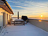 Dachterrasse mit Schnee im Sonnenuntergang über dem Hainer See. Am Ende der Terrasse stehen eine Sitzbank, ein Tisch mit Sesseln, ein Sonnenschirm und ein Strandkorb.