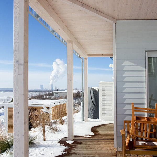 Holzterrasse mit Schnee, die um die Hausecke läuft.