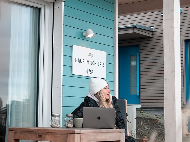 Frau in Winterkleidung auf Terrasse mit Tee und Laptop