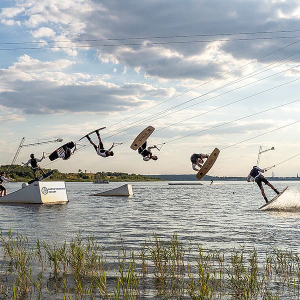 PErson auf einem Wakeboard fährt eine Rampe im Wasser hoch und macht einen Salto.