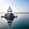 Mitten im Wasser ragt eine schwimmende Insel in Form eines Kirchturms aus dem Wasser.