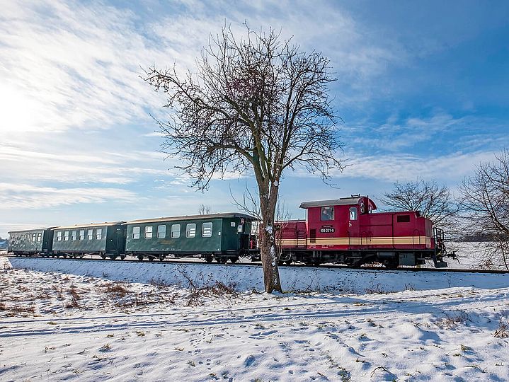 Rote Diesellok mit grünen Wagen fährt durch verschneite Landschaft